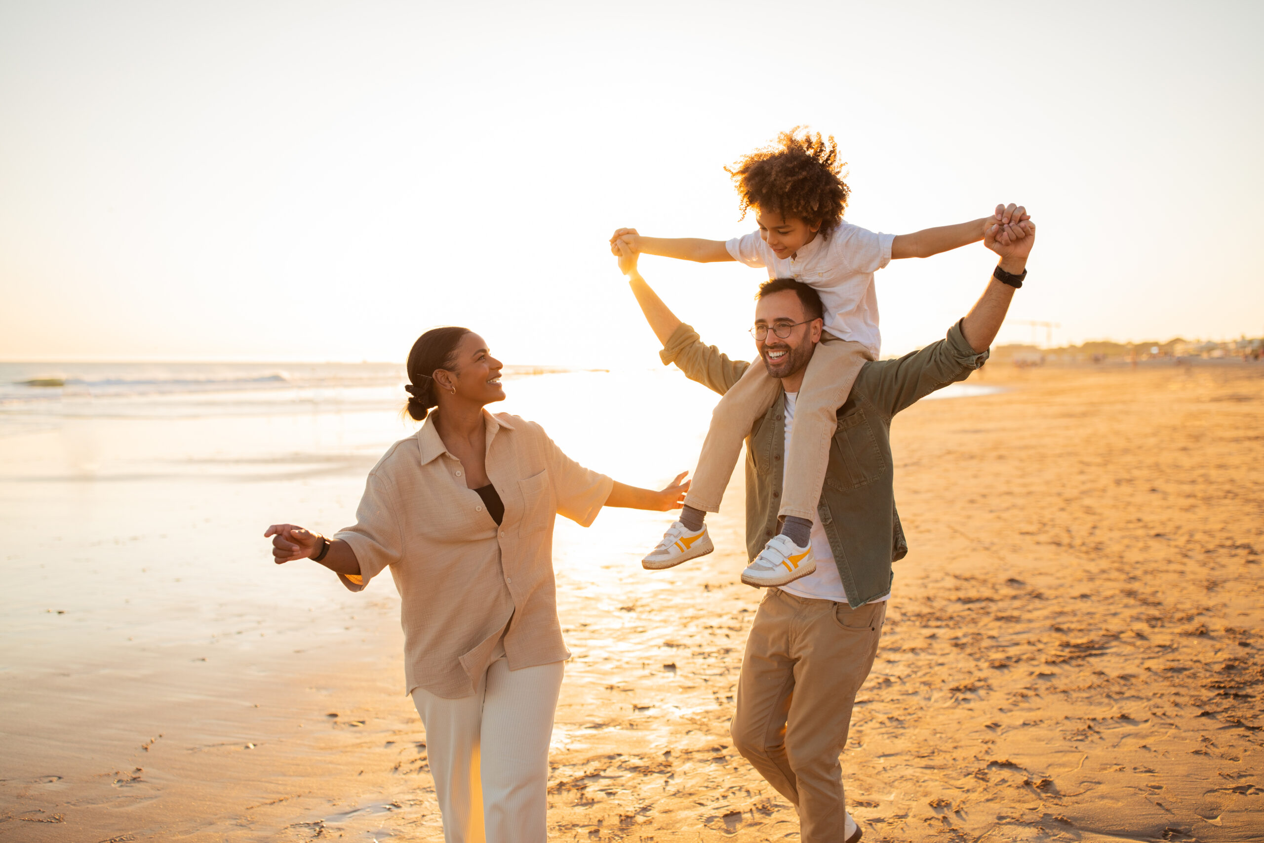 family of mom and dad and young son on the beach with the son on the dads shoulders