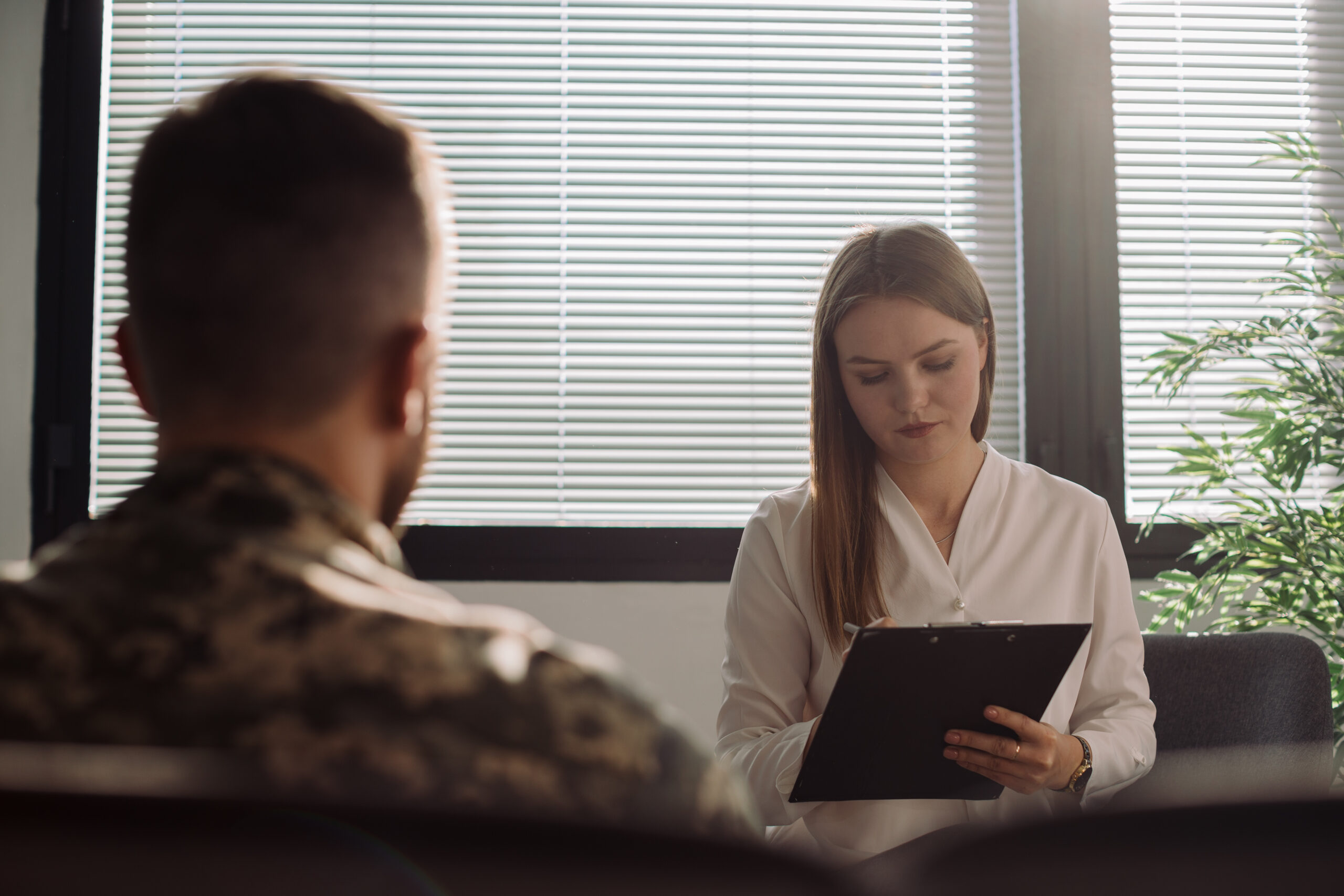 male veteran getting psychotherapy from a woman therapist with a clipboard