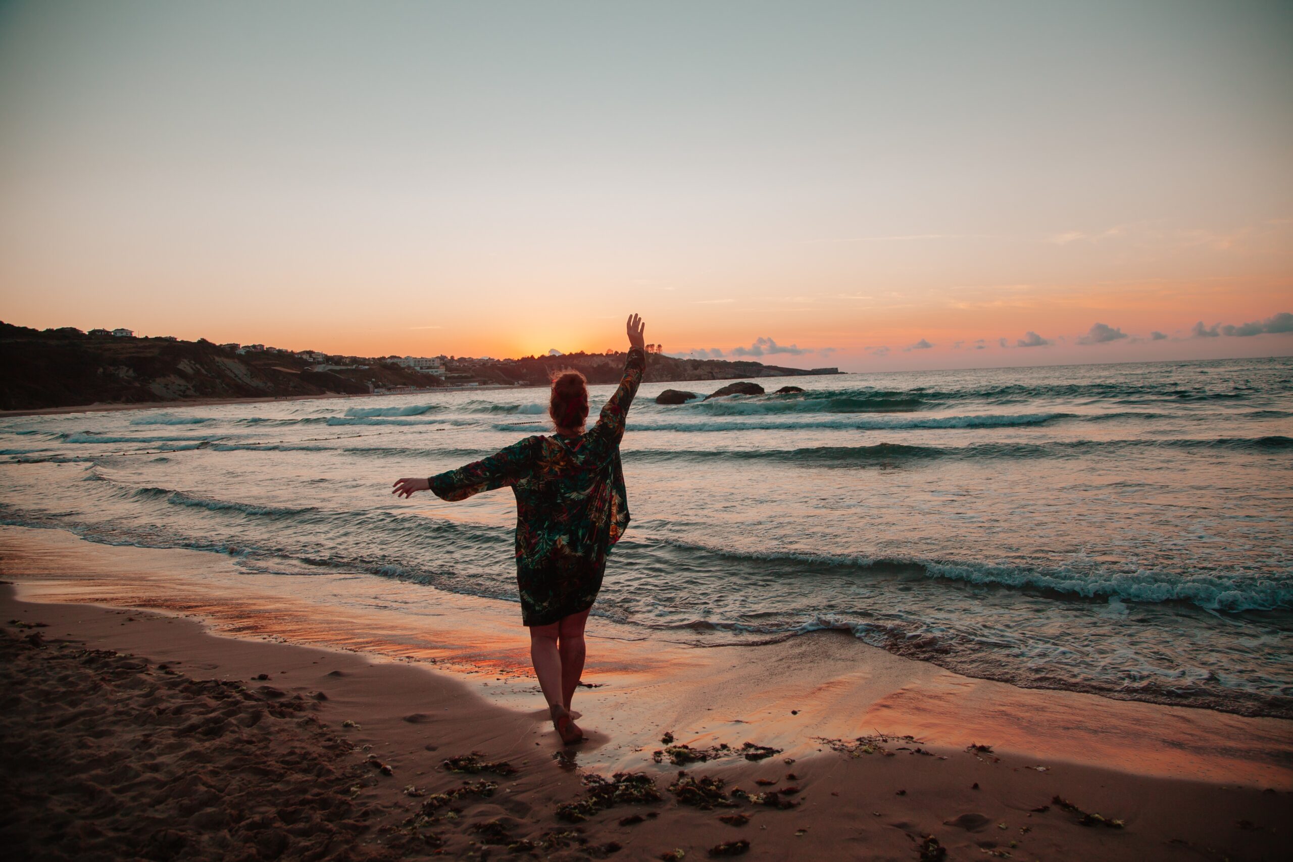 sunset on the beach with person standing with their arm up silhouette