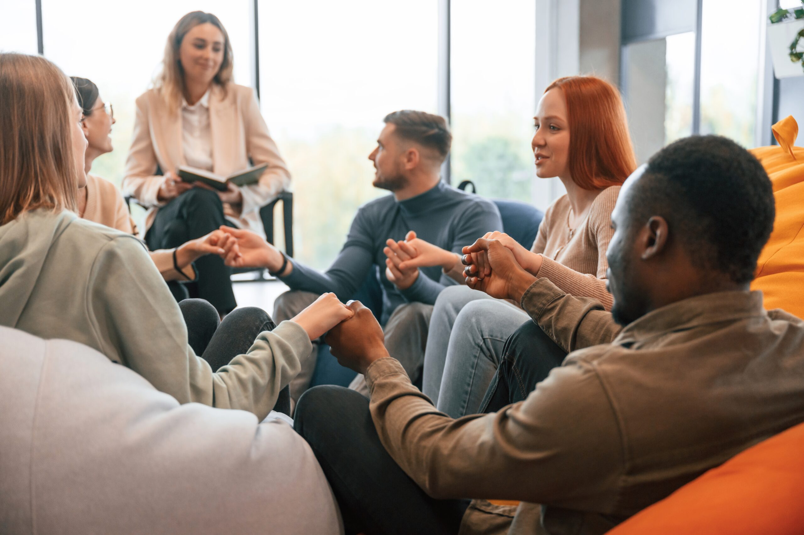 Sitting and holding each other by hands. Group of people are having therapy meeting together.