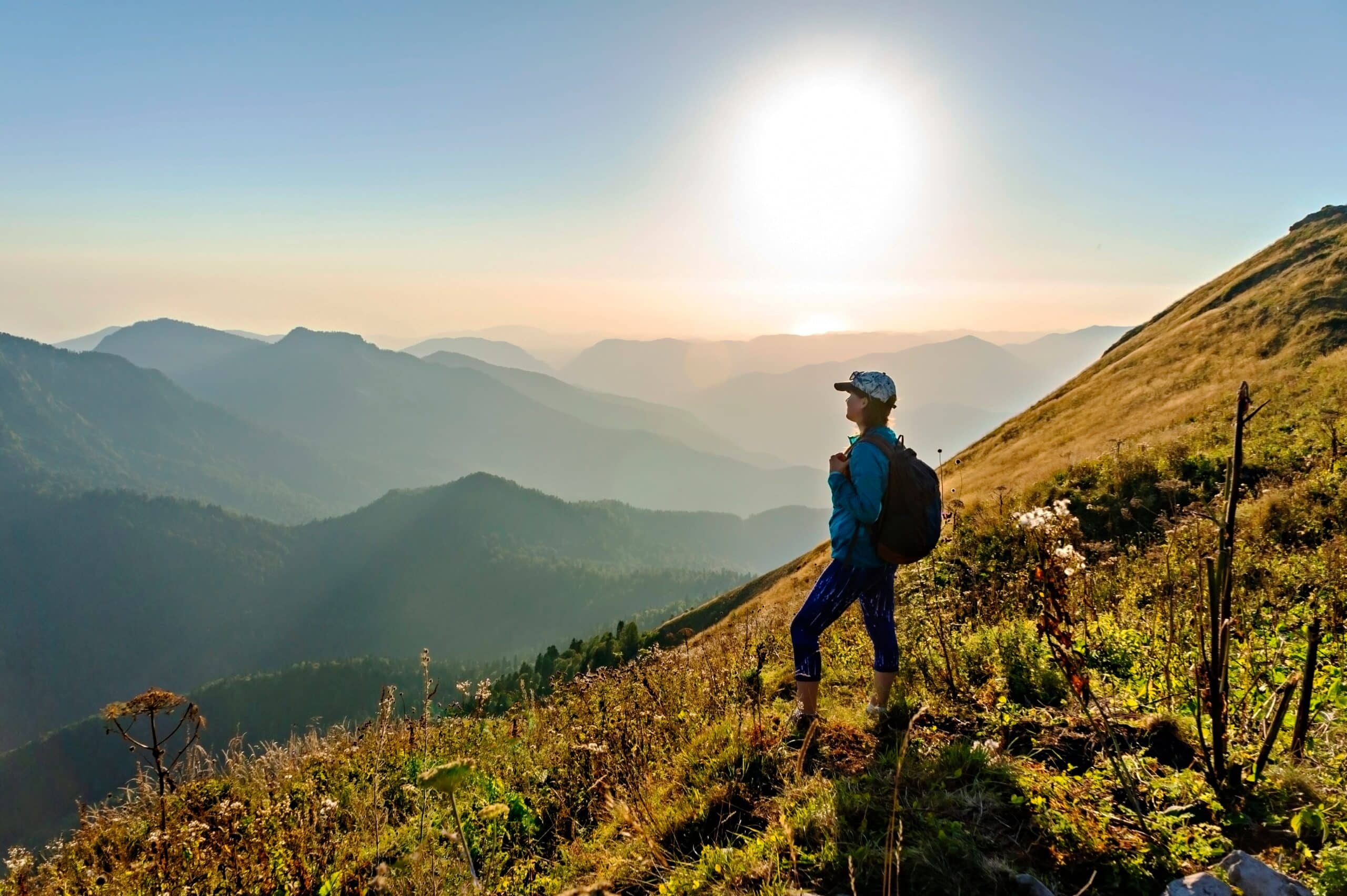 woman standing on a cliff looking at mountains on a hike at sunrise
