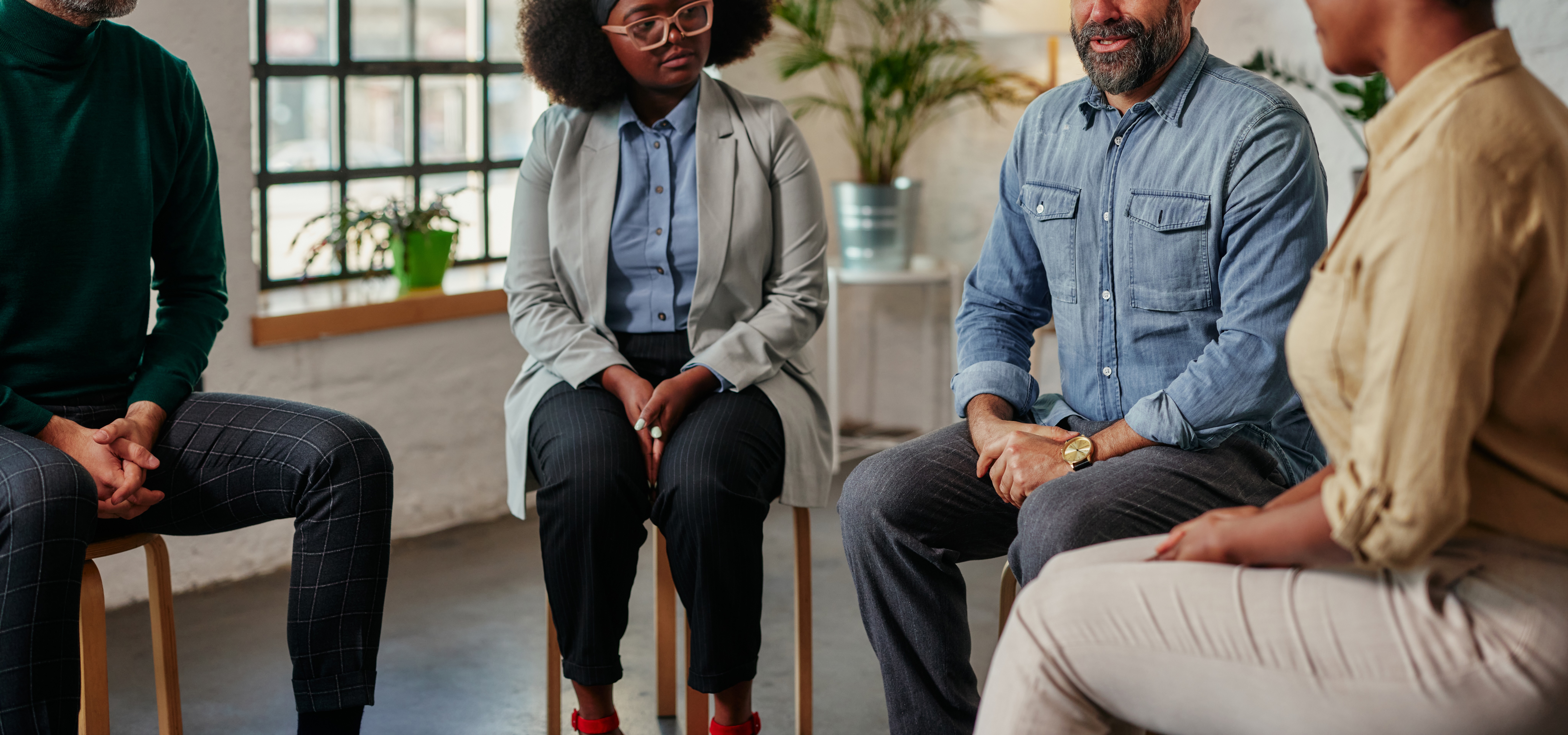 A diverse group of people sitting on chairs in a circle and discussing some problems together during the therapy session.