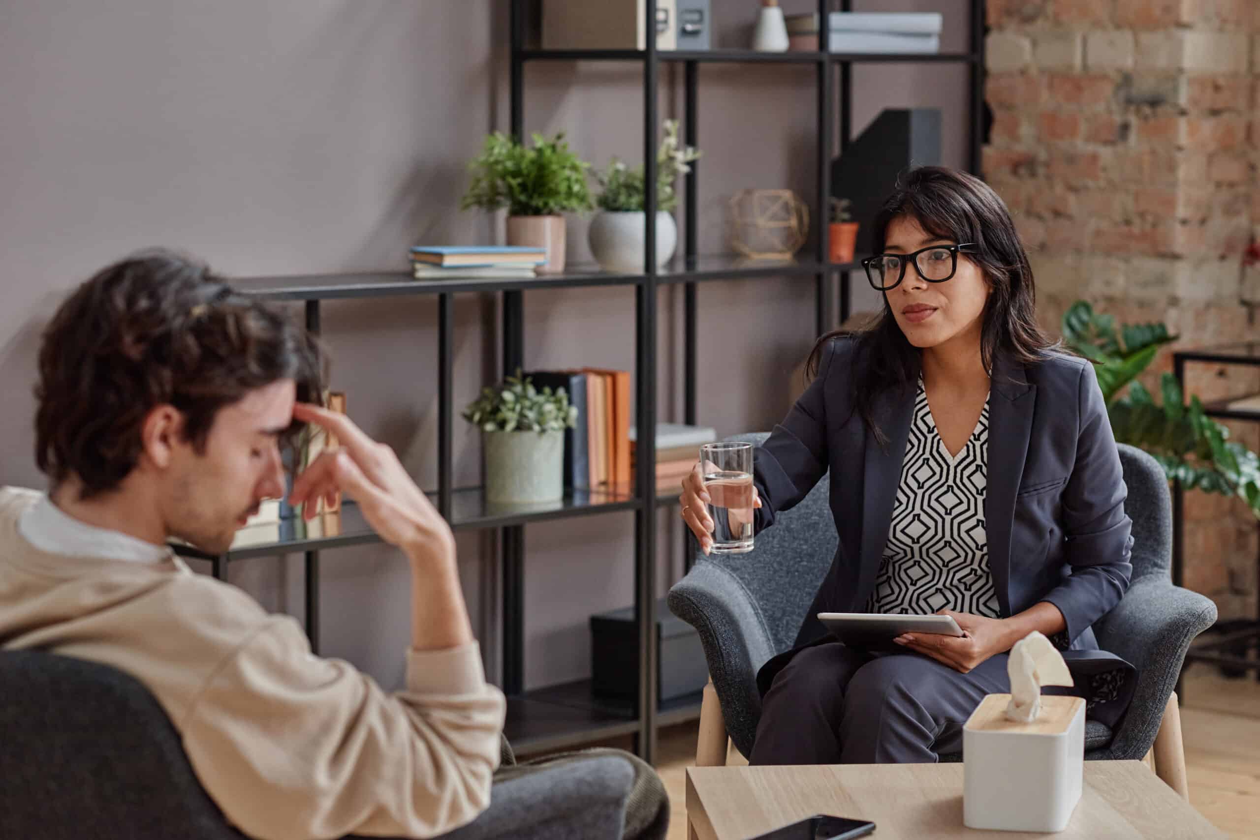 Horizontal medium shot of professional psychotherapist offering her client glass of water to calm down