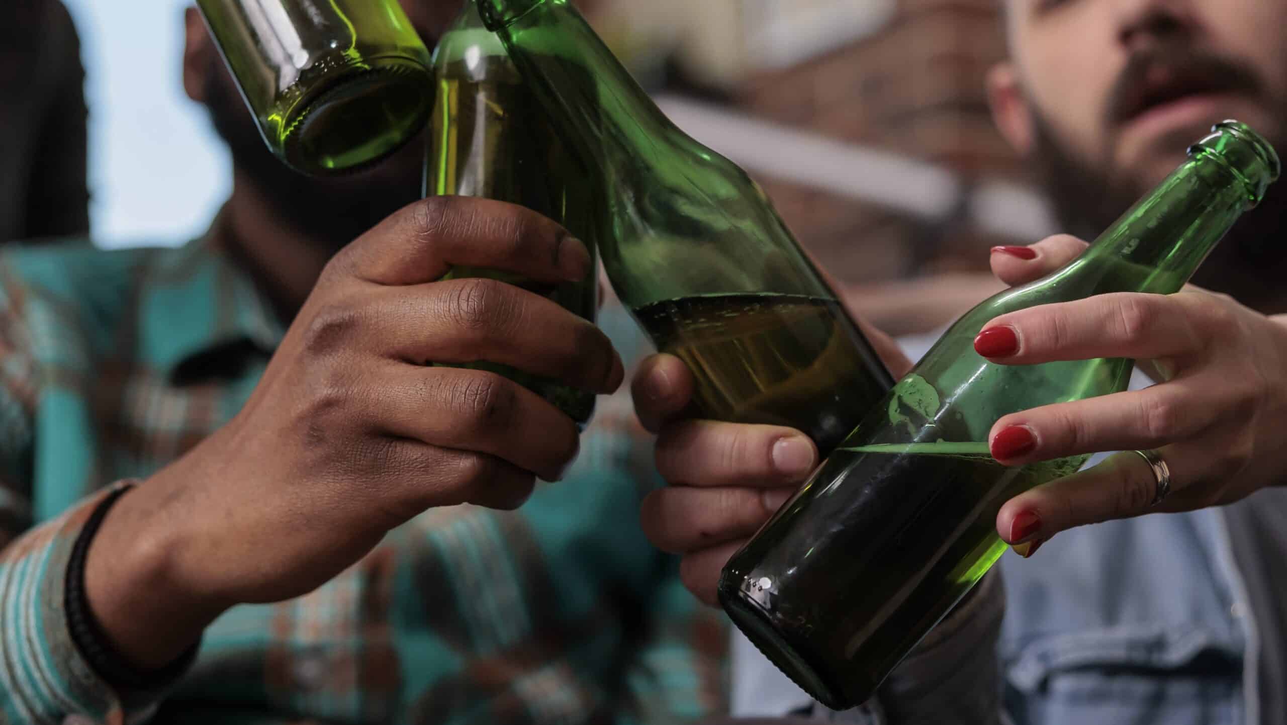 Multiethnic group of friends saying cheers and clinking beer bottles to celebrate party event, feeling happy about reunion. People toasting with alcohol drinks at hangout, leisure activity. Close up.