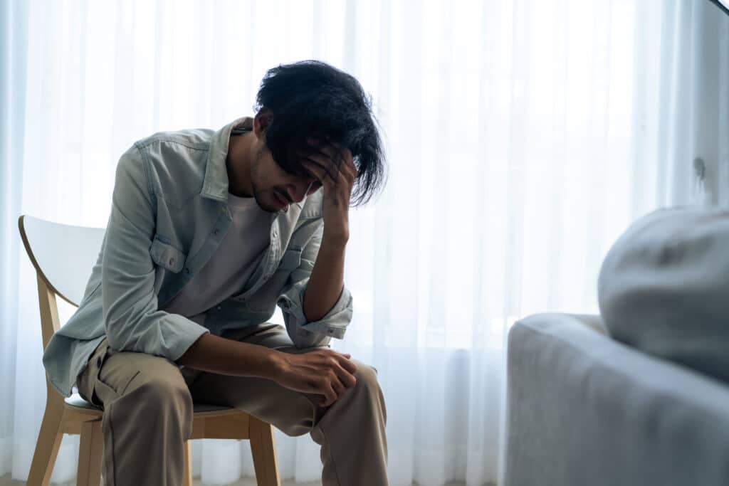 Asian young upset depressed man sitting alone in living room at home. Attractive unhappy male feeling very sad, lonely and frustrated with life problem think of money debt, budget loss, bankruptcy.