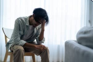 Asian young upset depressed man sitting alone in living room at home. Attractive unhappy male feeling very sad, lonely and frustrated with life problem think of money debt, budget loss, bankruptcy.