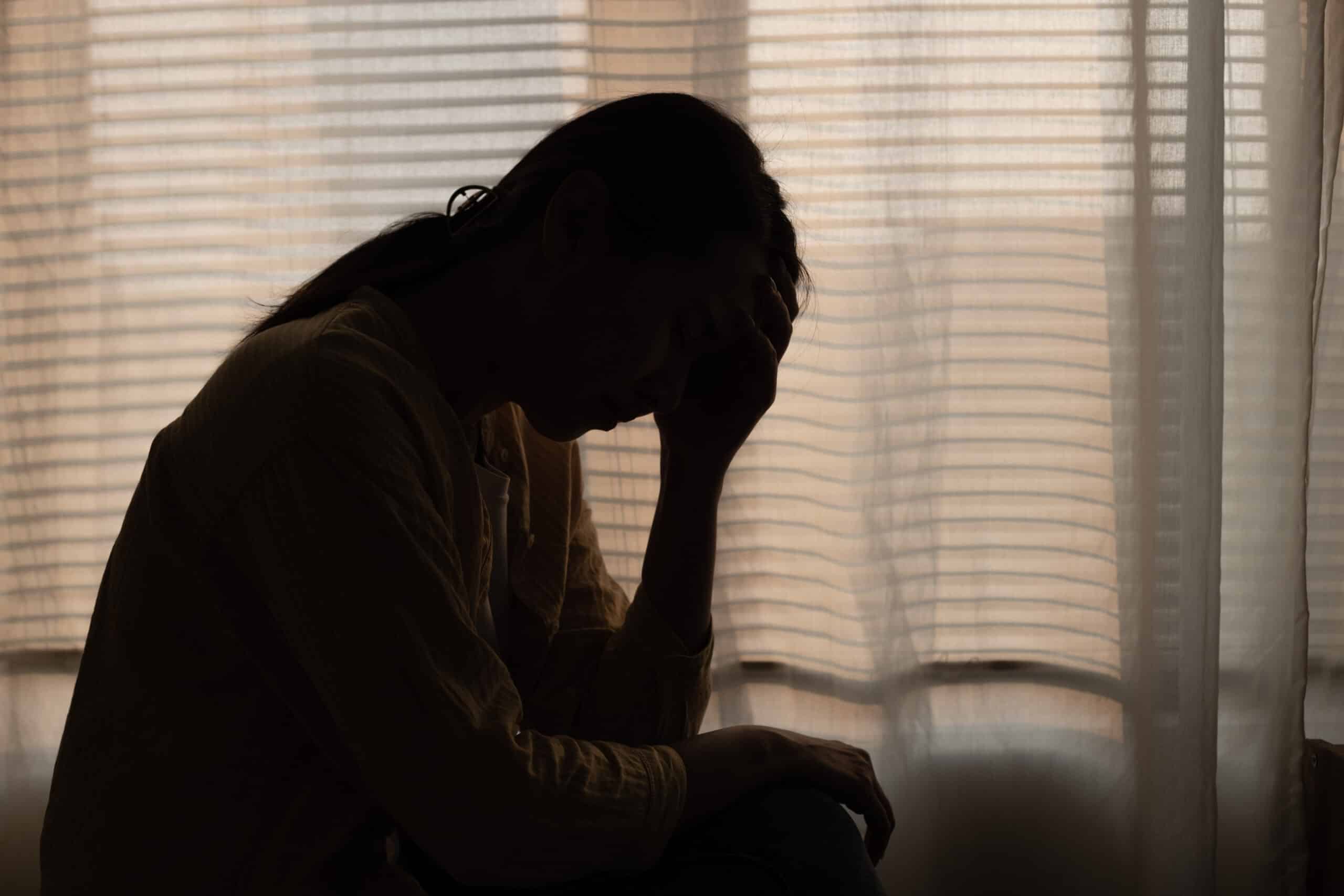 Female having depression sitting alone in bedroom dark corner. woman headache unhappy emotion. young anxiety despairing mental health problems. Dark Tone.