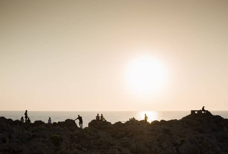 Silhouette of people on rocks at sunset, Ciutadella, Menorca, Spain