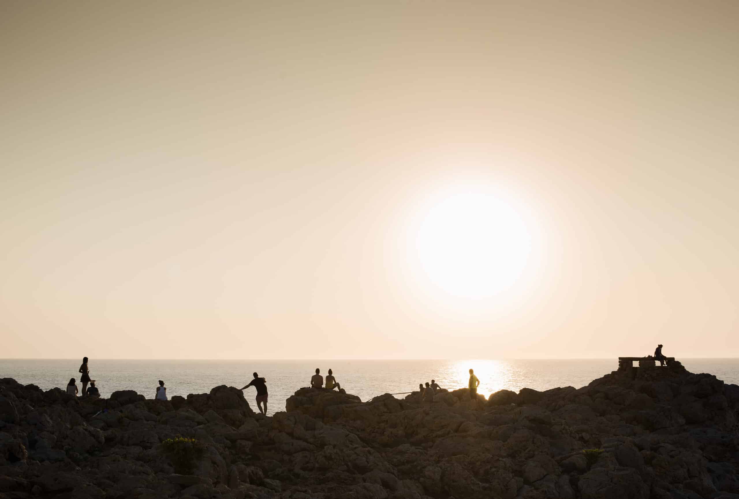 Silhouette of people on rocks at sunset, Ciutadella, Menorca, Spain