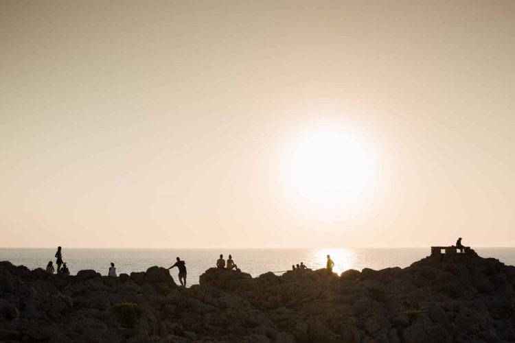 Silhouette of people on rocks at sunset, Ciutadella, Menorca, Spain